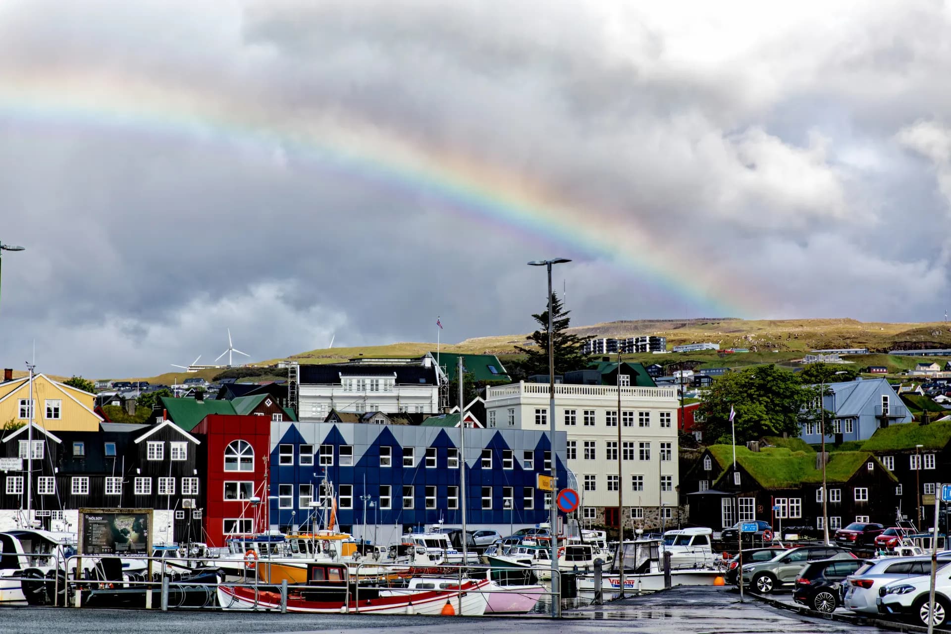 Rainbow over colorful buildings and harbor with boats.