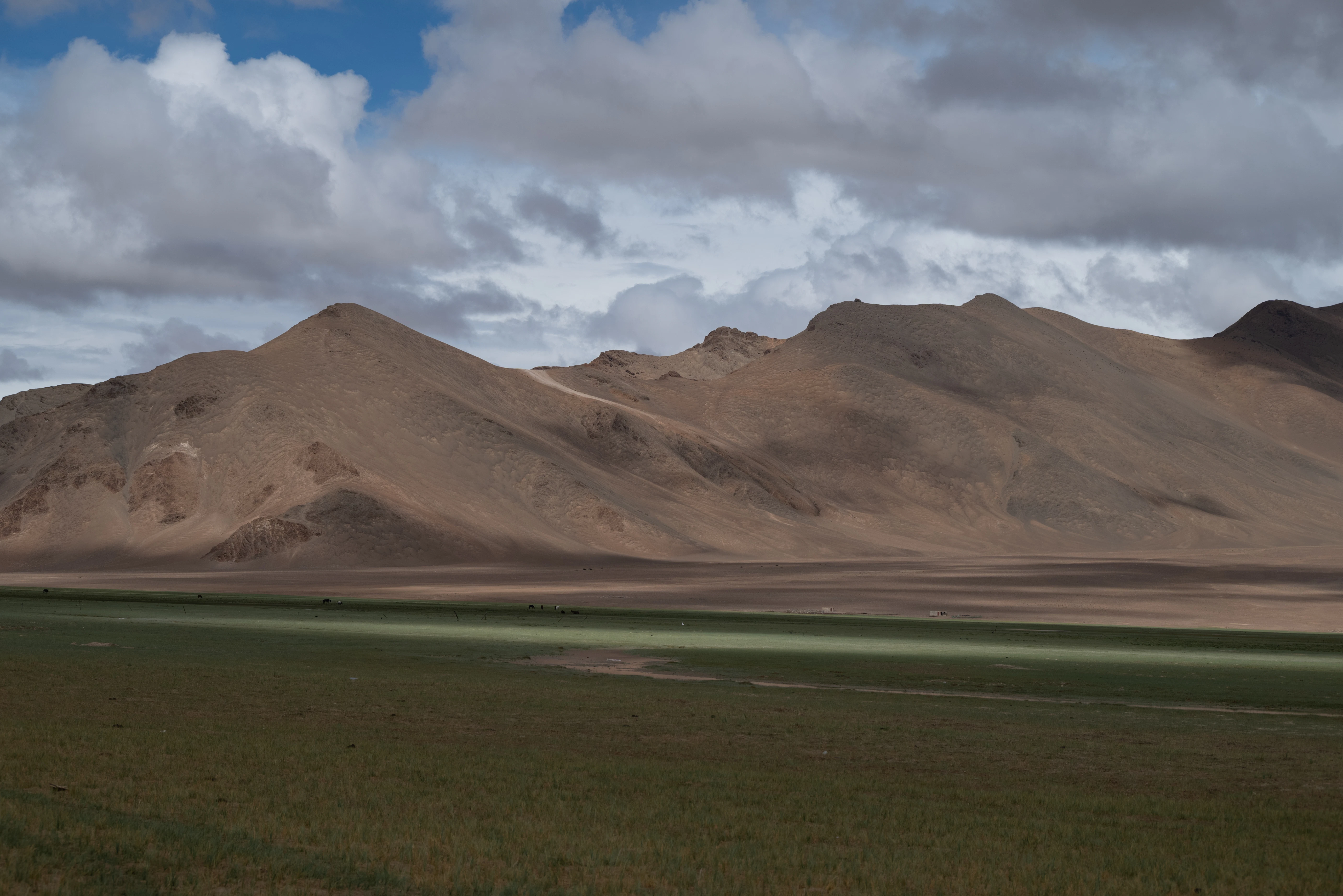 Barren mountains under a cloudy sky with green field.
