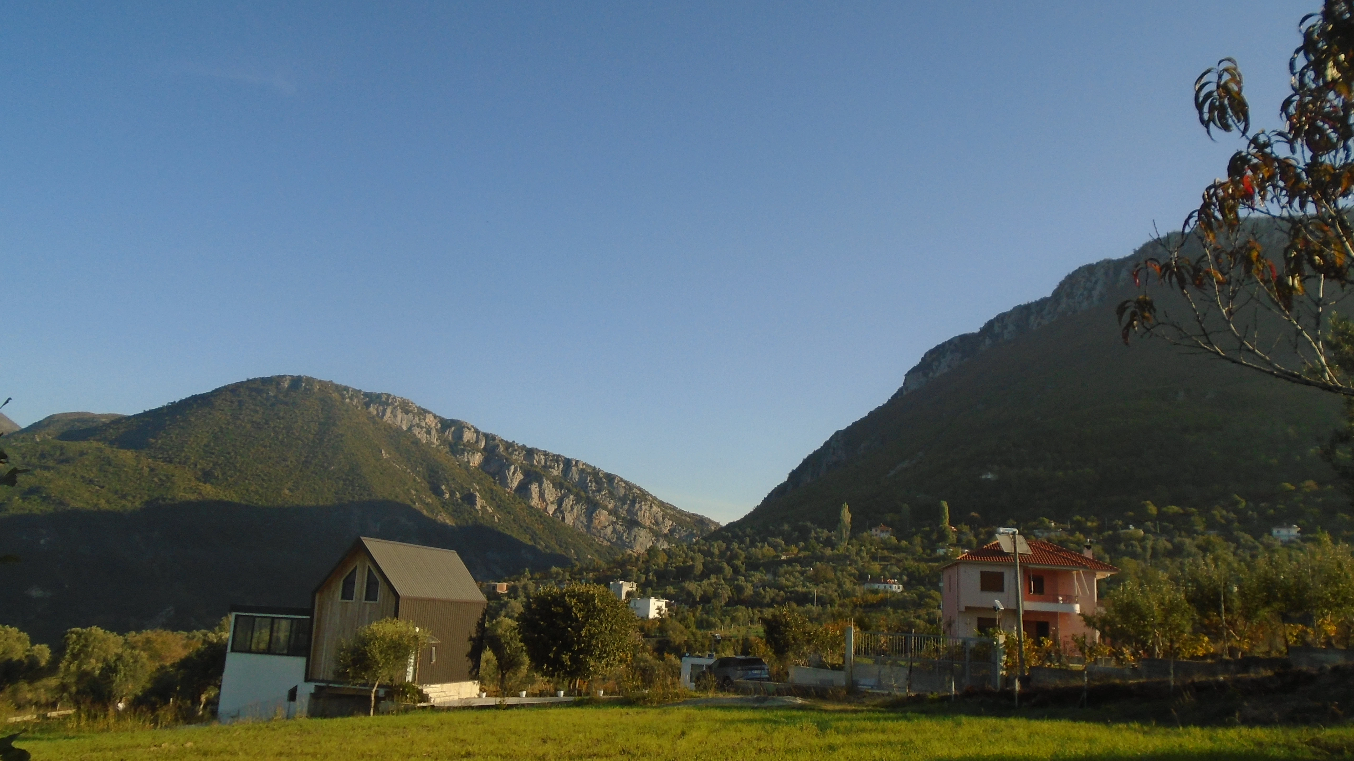 A grassy field with a house and mountains in the background